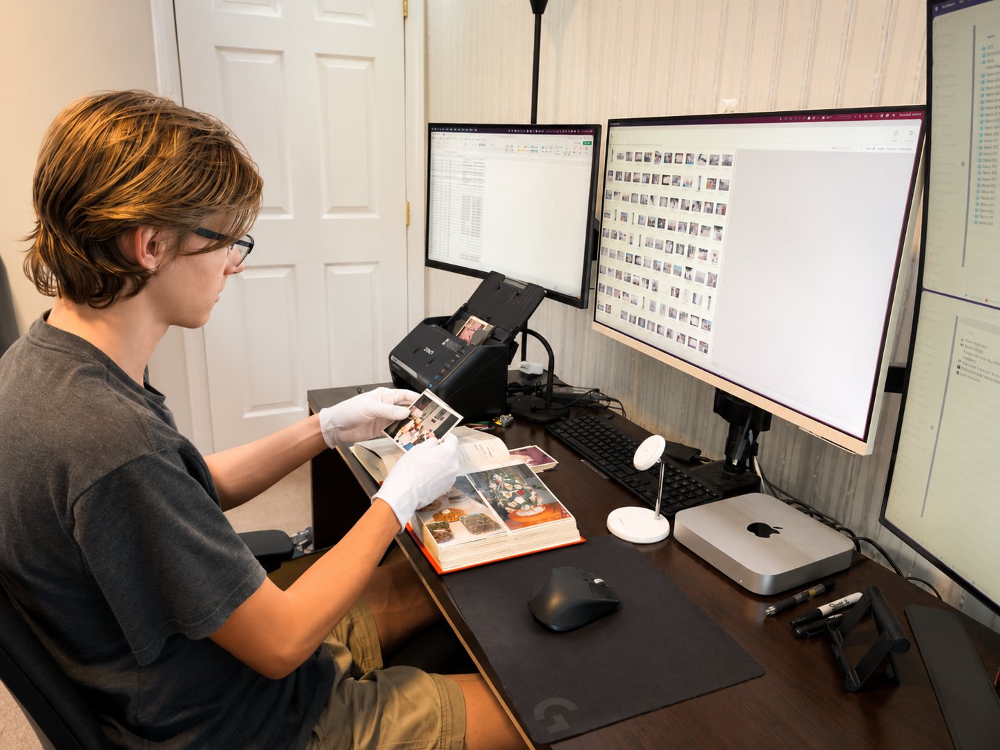 An archivist at the Severna Park scanning bench, reviewing a worn family album beside an Epson photo scanner and dual monitors