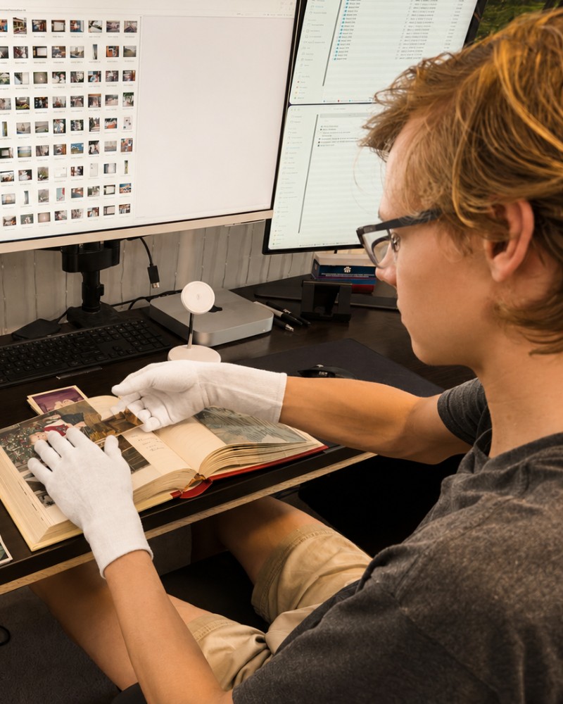 The archivist at the Severna Park bench, turning the pages of a family album in cotton gloves beside the scanning monitors